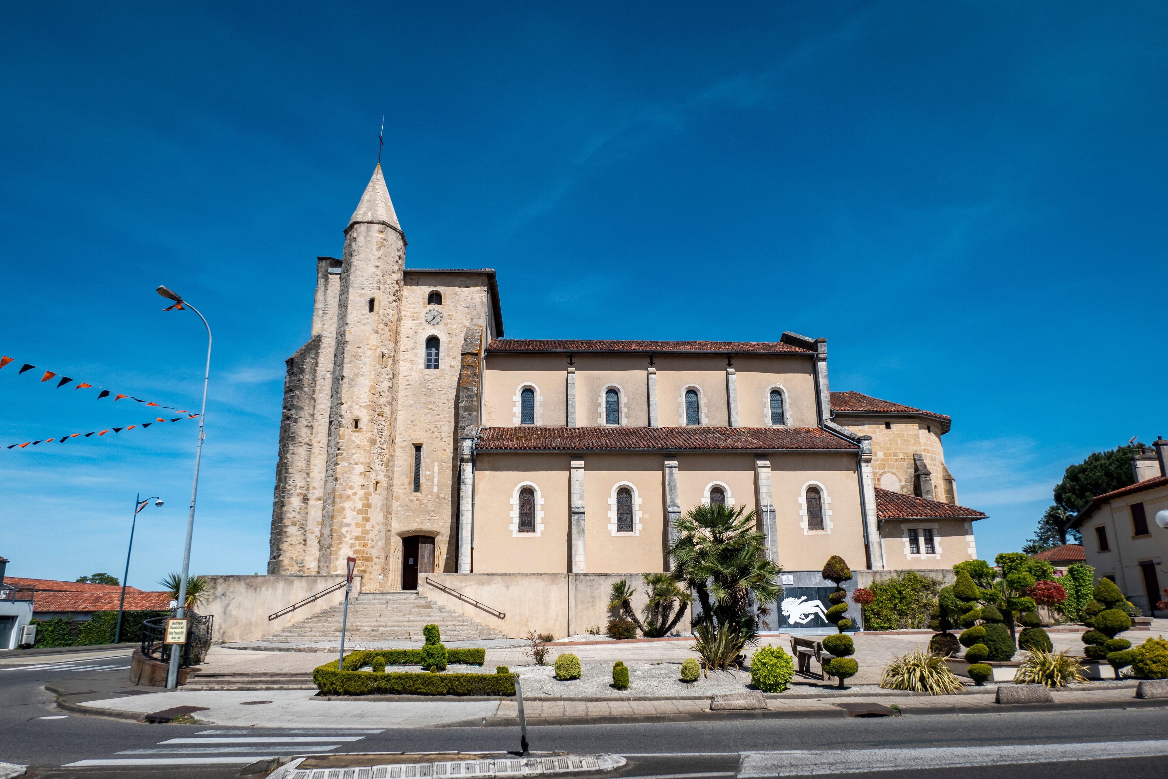 A historic church with a tall bell tower and a well-maintained garden in front.
