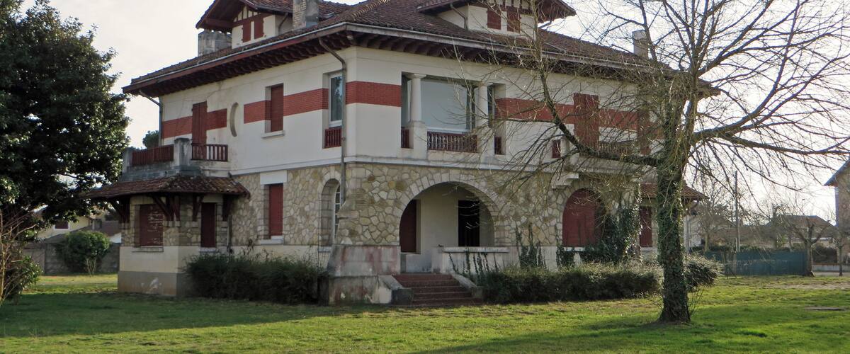 A two-story house with a stone facade, red shutters, and a tiled roof.