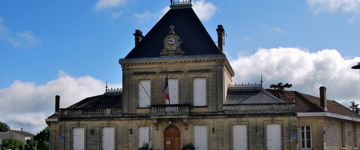 A historic building with a clock tower, a flag, and a well-maintained garden.