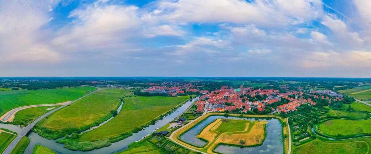 A town with red-roofed houses, surrounded by green fields and a river.