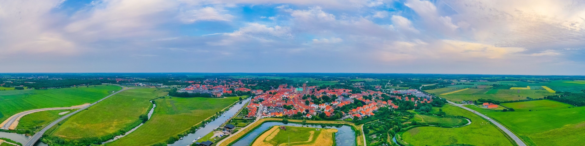 A town with red-roofed houses, surrounded by green fields and a river.