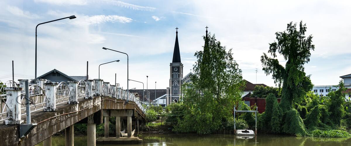A bridge over a river with a church steeple in the background.