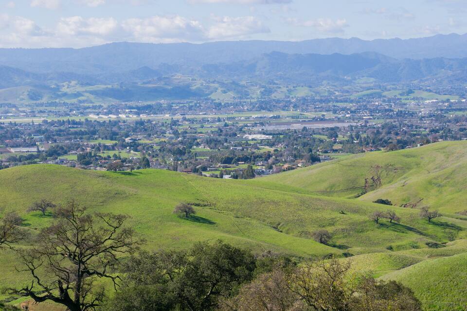 Rolling green hills, a distant town, and mountains in the background.