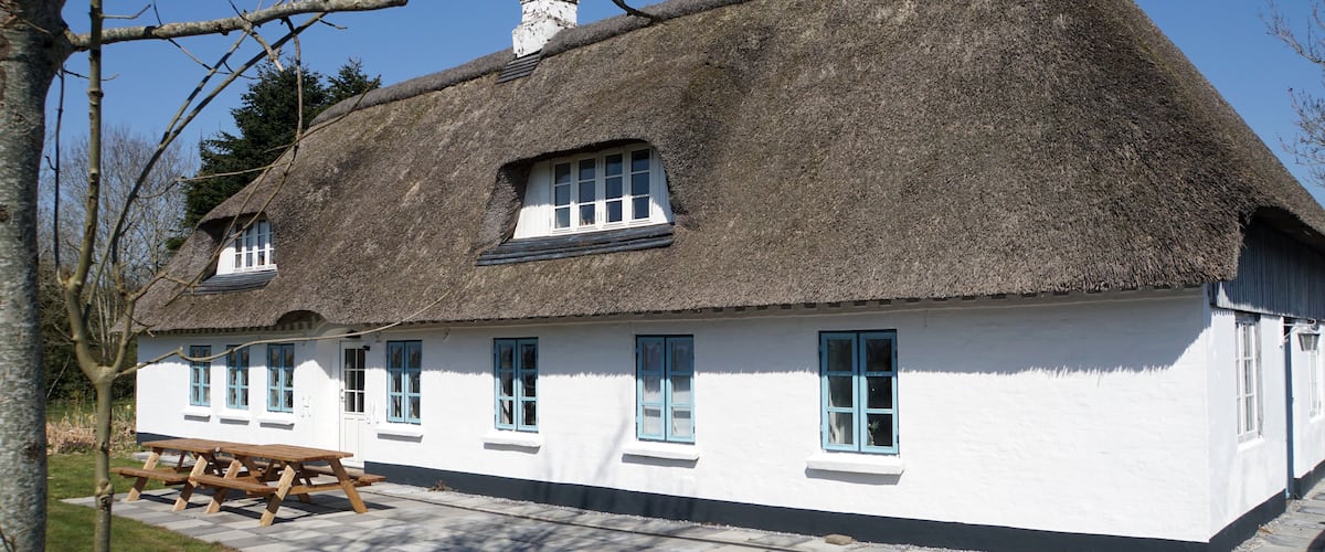 A thatched-roof house with white walls and multiple windows.