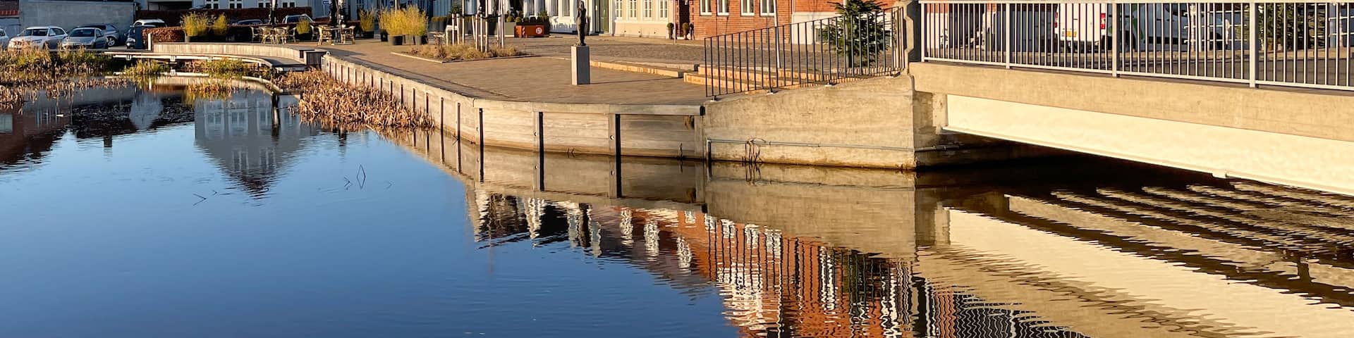 A canal with buildings reflecting on the water, a pedestrian bridge, and a speed limit sign.