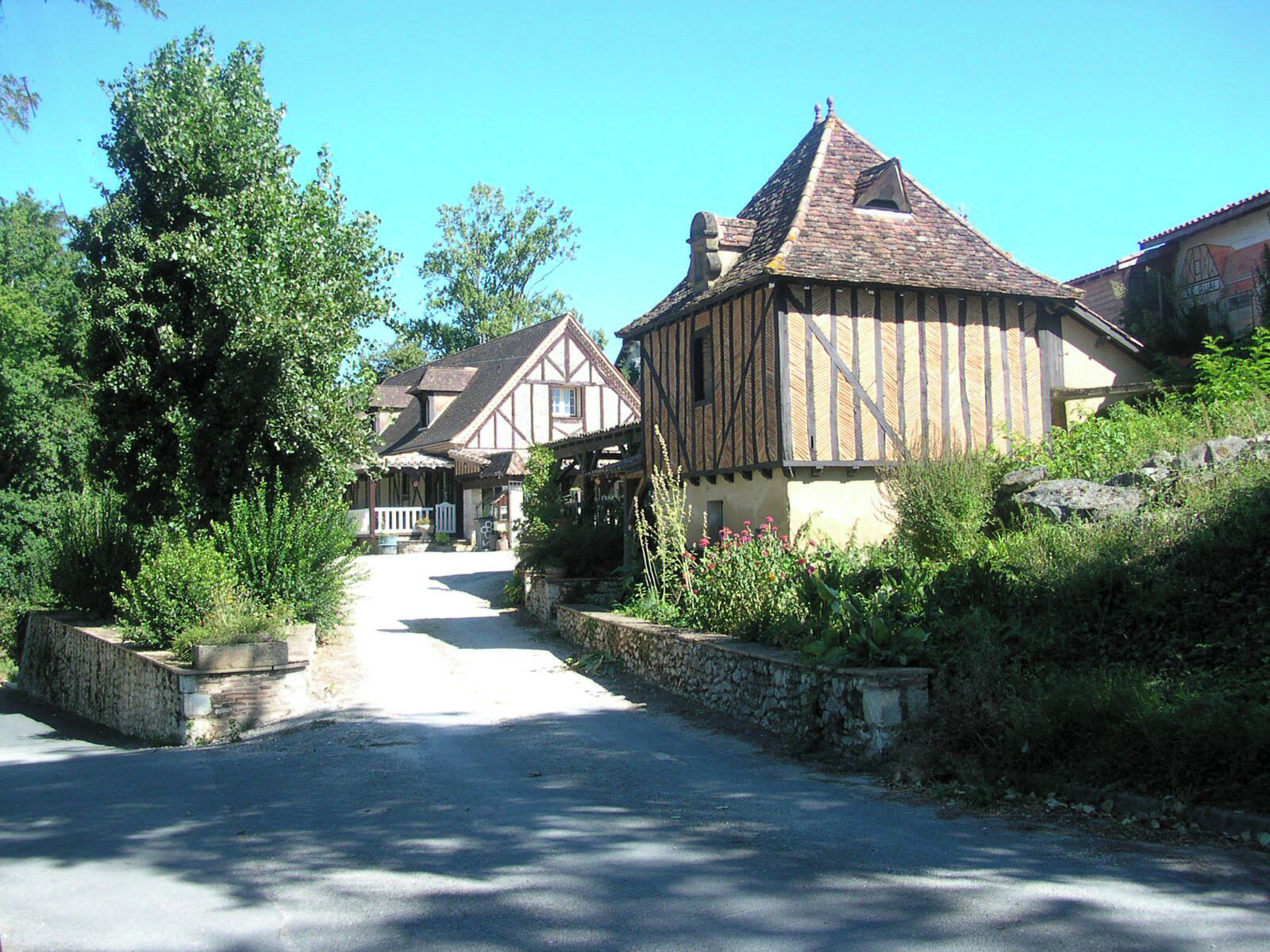 A narrow road flanked by traditional timber-framed houses with stone walls and lush greenery.