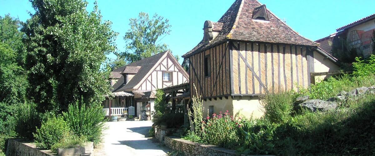 A narrow road flanked by traditional timber-framed houses with stone walls and lush greenery.