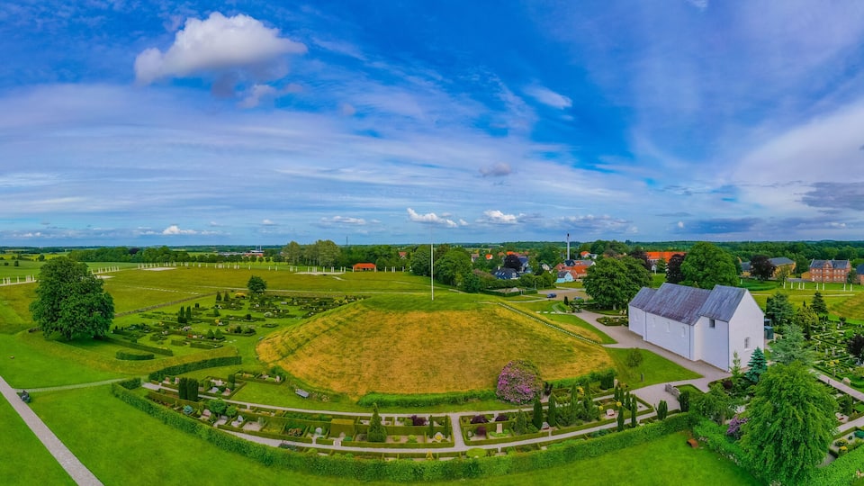 A large green park with a white building, a yellow house, and a red-roofed house.