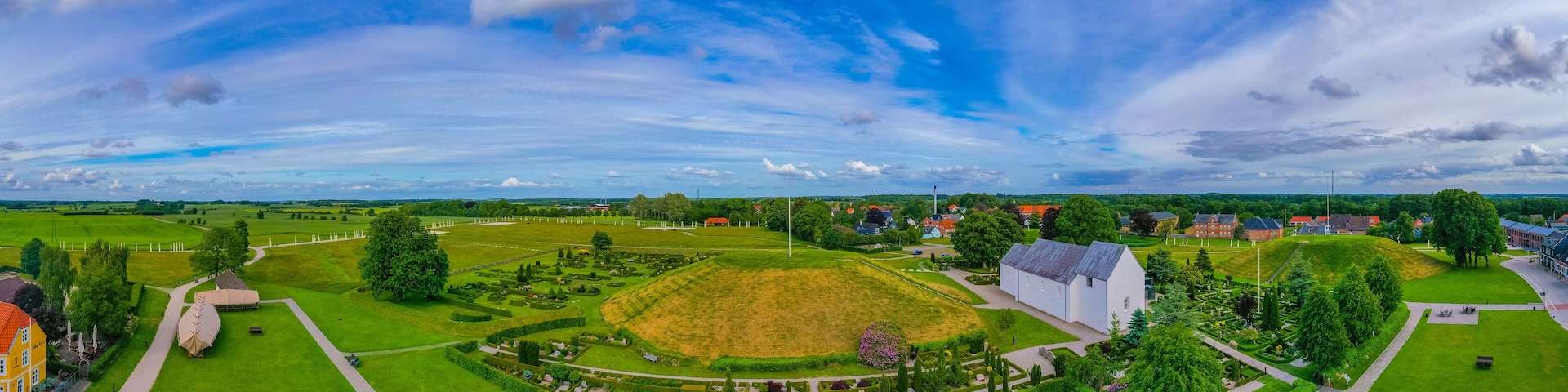 A large green park with a white building, a yellow house, and a red-roofed house.