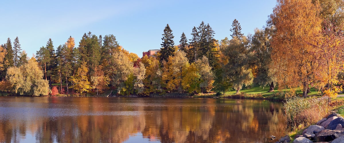 A calm lake surrounded by autumn trees and a building in the background.