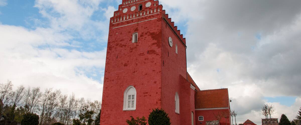 A red church with a clock tower, stone wall, and steps leading to the entrance.