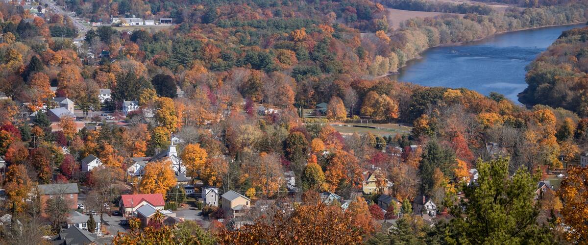 A town nestled by a river, surrounded by autumn-colored trees.