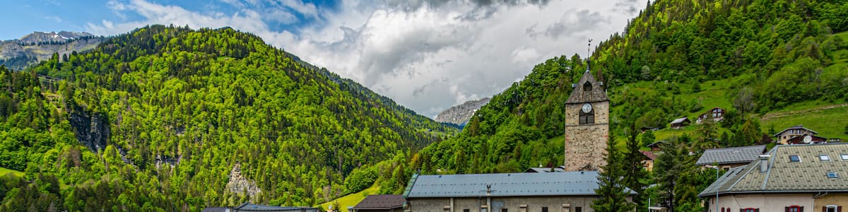 A mountainous village with colorful buildings, a stone bridge, and a church with a bell tower.