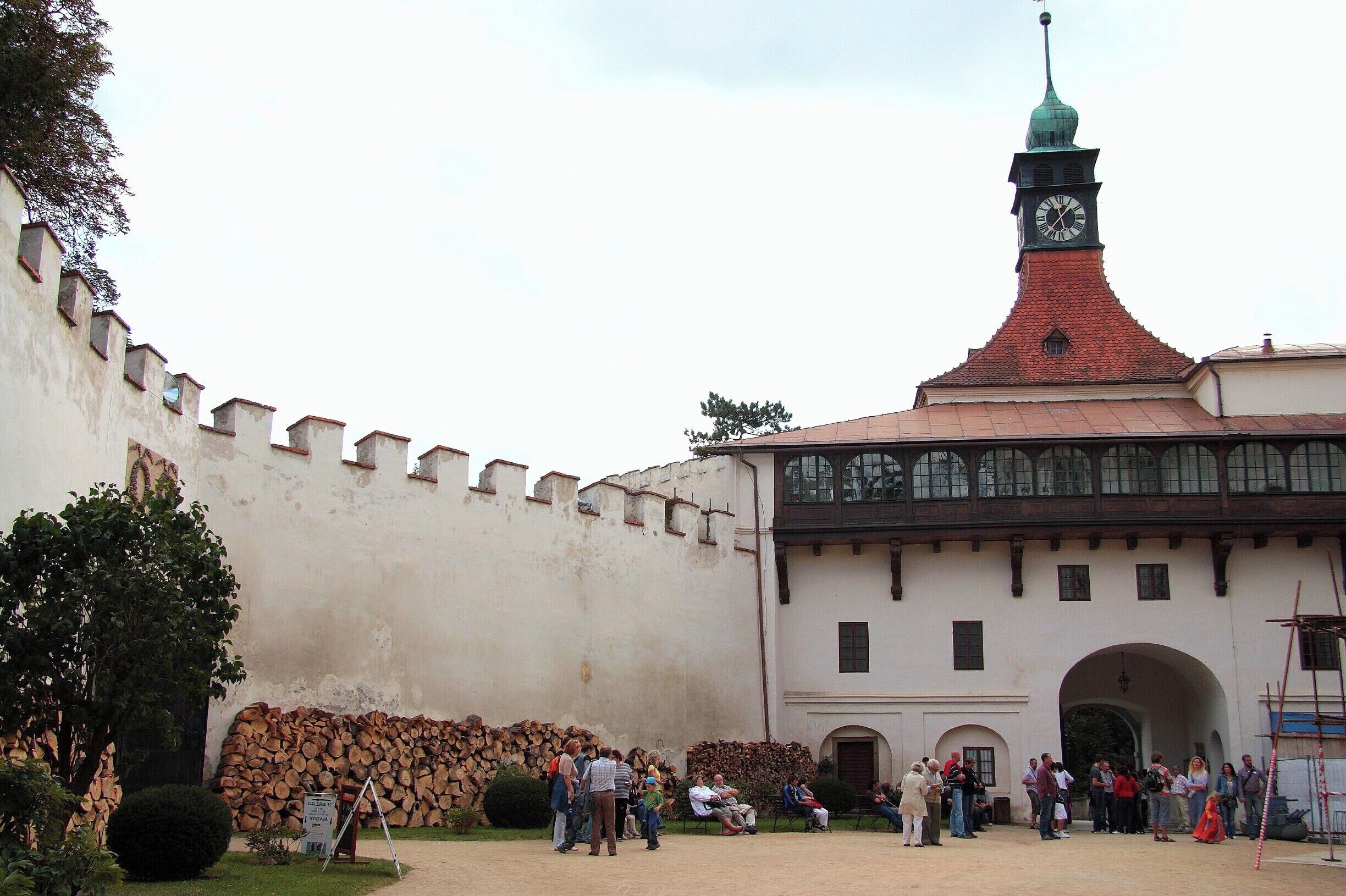 A historic building with a clock tower, a stone wall, and a group of people gathered in front.
