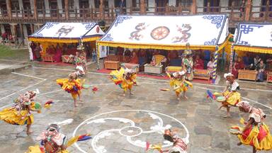 A group of dancers in traditional attire performing in front of a temple with colorful banners.