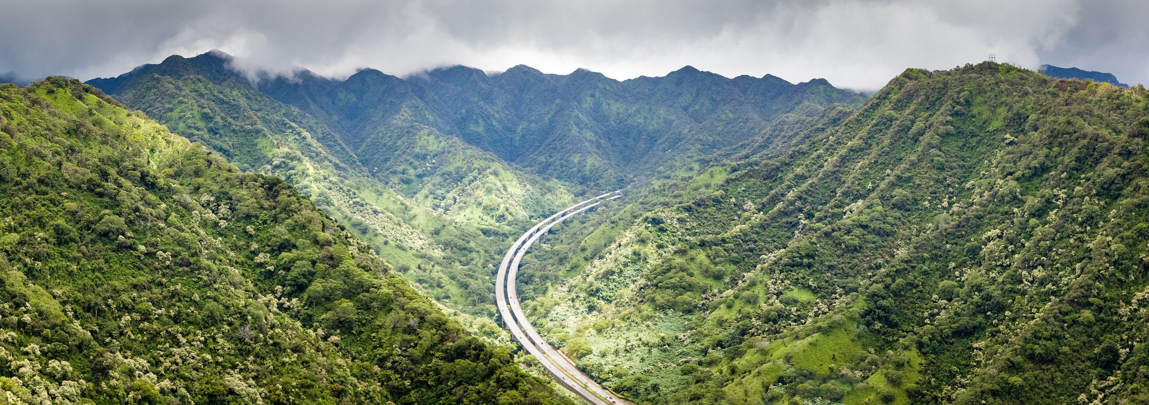 A winding road through a lush, green valley with mountains in the background.