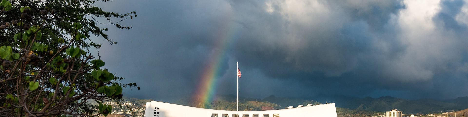 A boat with a rainbow, a flag, and a cityscape in the background.