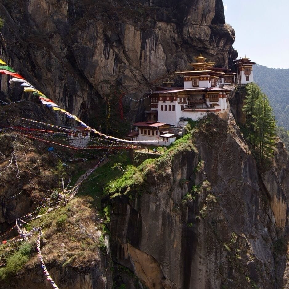 A monastery perched on a cliffside with a rope bridge.