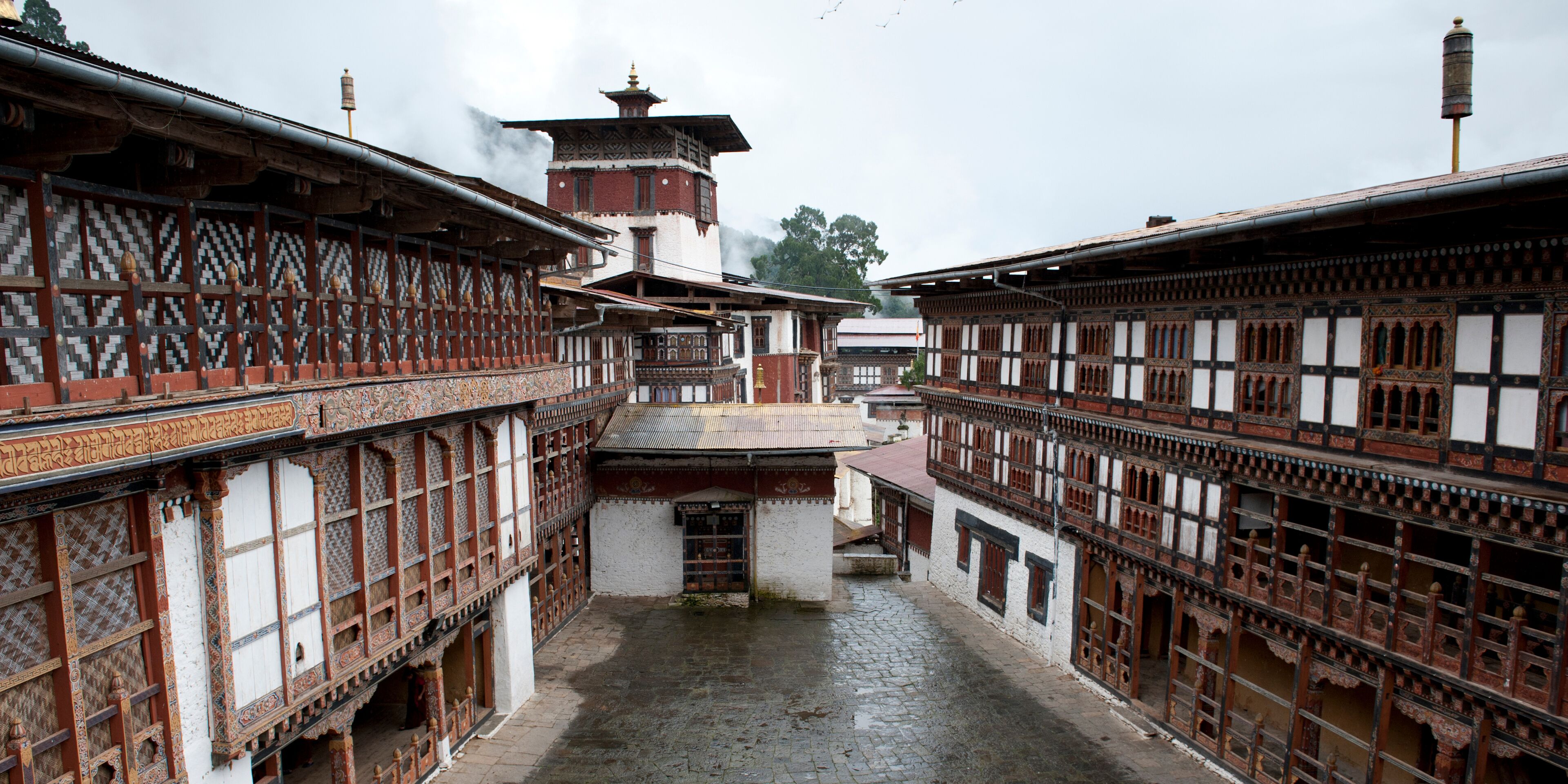 A traditional courtyard with ornate buildings, a tower, and a cobblestone path.