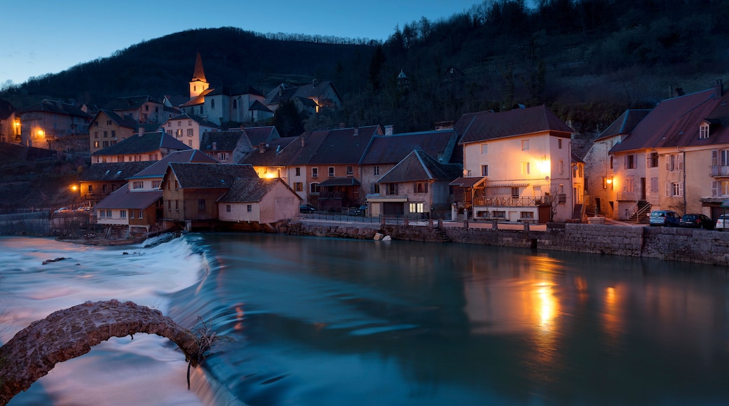 Un paese sul fiume al crepuscolo, con edifici illuminati e un fiume che scorre.