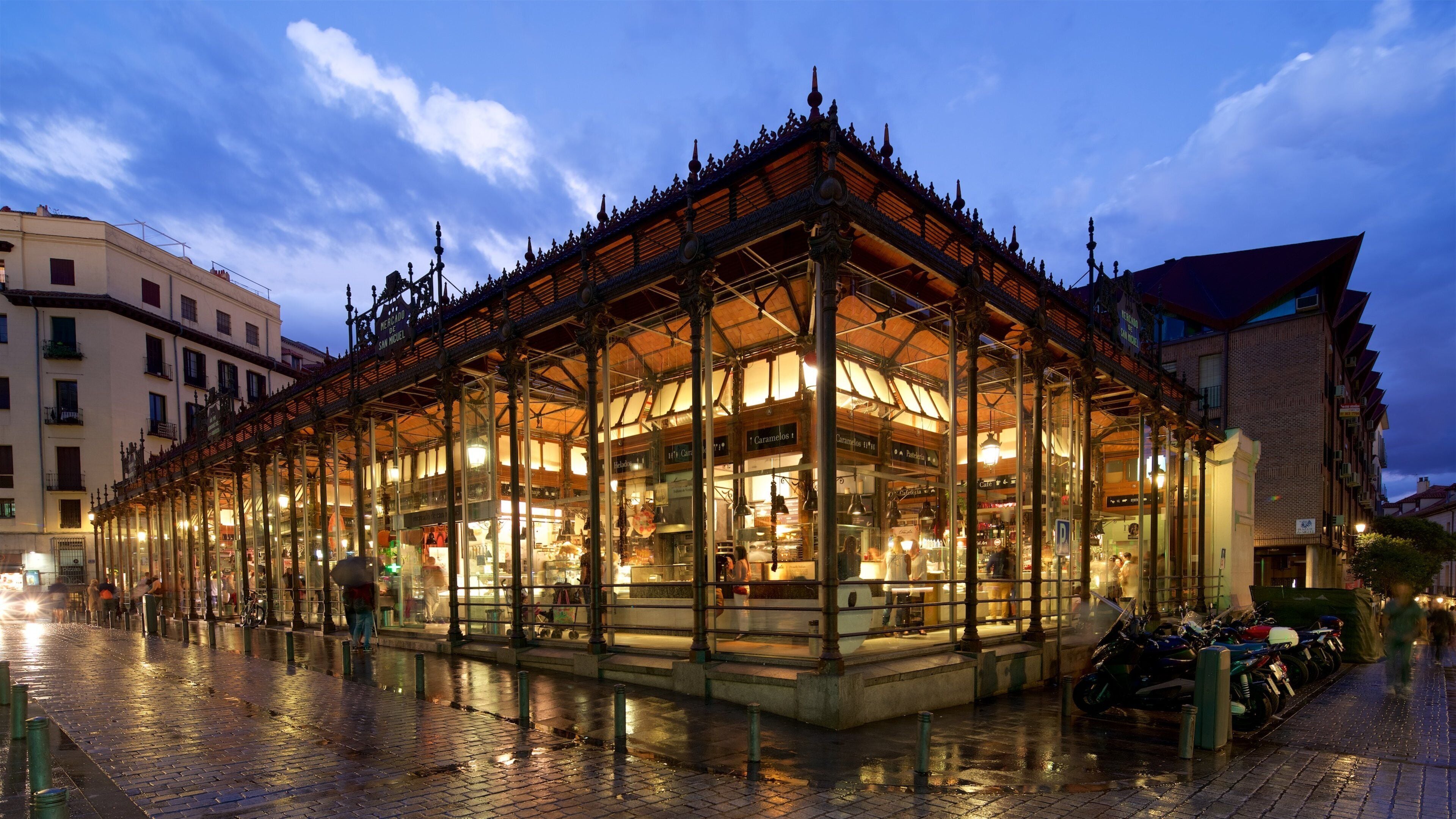 Um edifício histórico de mercado com cobertura de vidro, grades de metal elaboradas e pavimento de azulejos.