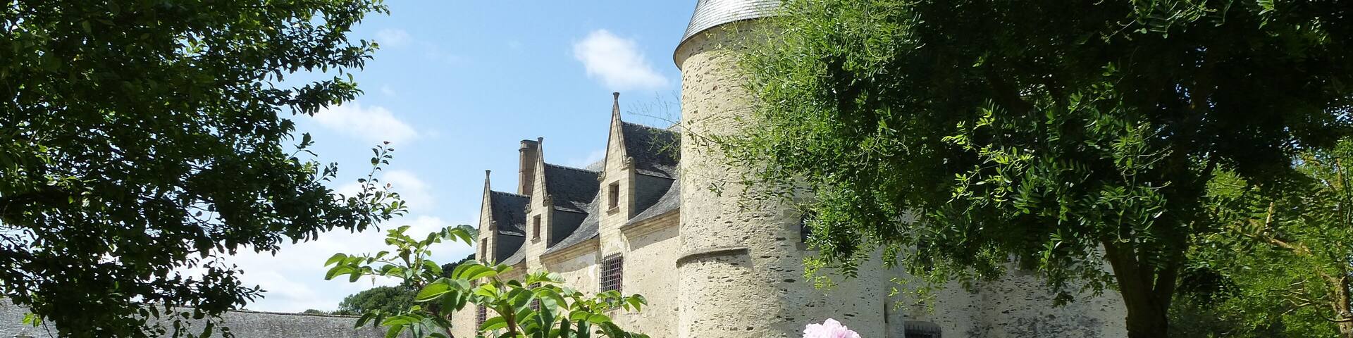 A historic building with a round tower and a garden with blooming flowers.