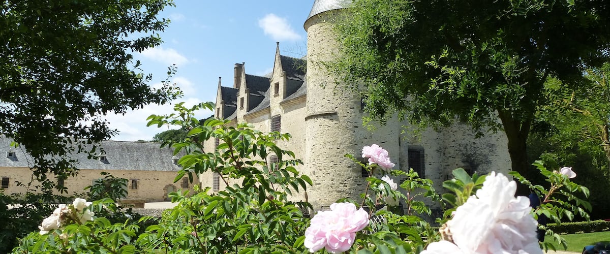 A historic building with a round tower and a garden with blooming flowers.