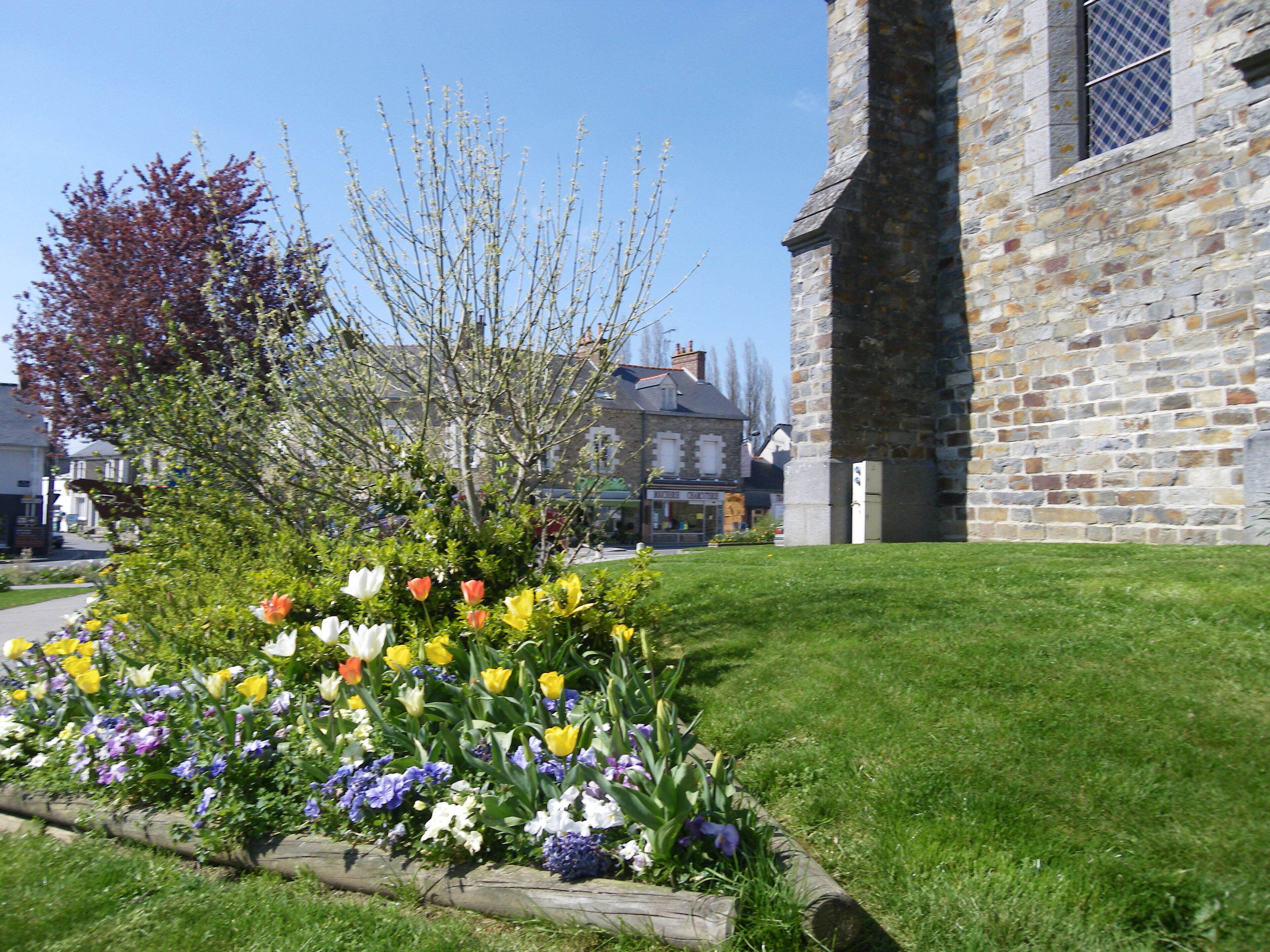 A stone building with a window, surrounded by a flower bed with various flowers.