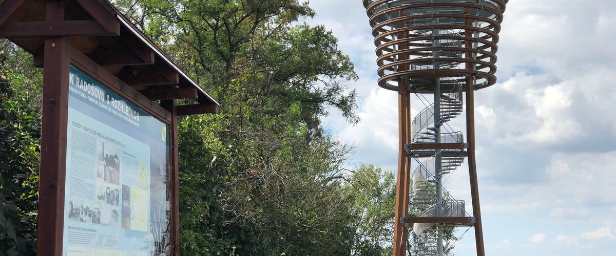 A metal tower with a spiral staircase, surrounded by trees and a signboard with historical information.