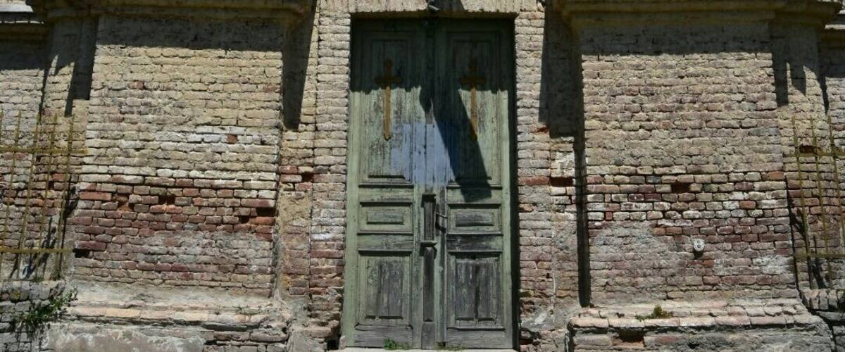 An old, weathered building with a large arched window and a wooden door.