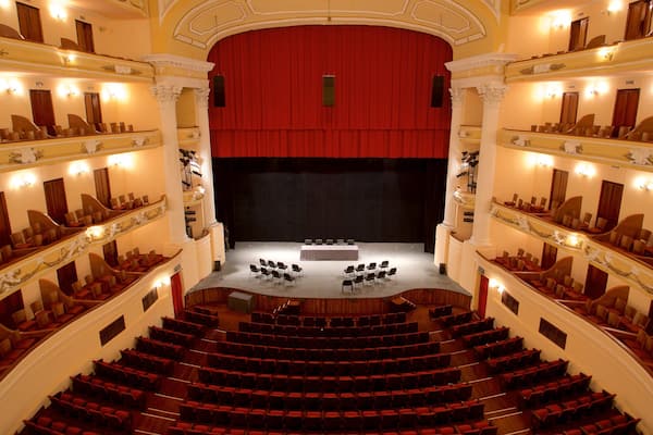 A grand theater with red curtains, multiple balconies, and rows of red seats.