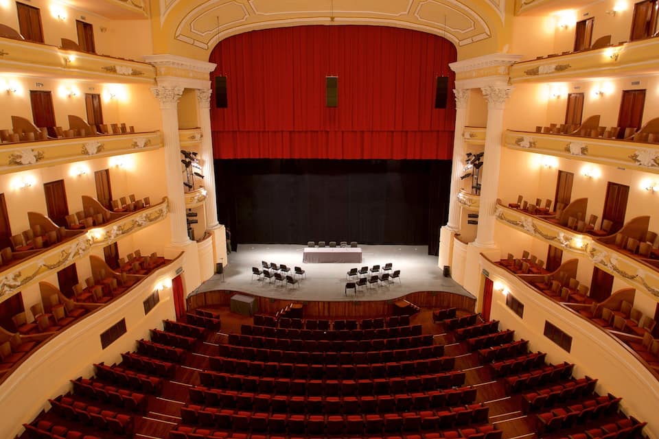 Um teatro imponente com cortinas vermelhas, várias galerias e fileiras de assentos vermelhos.