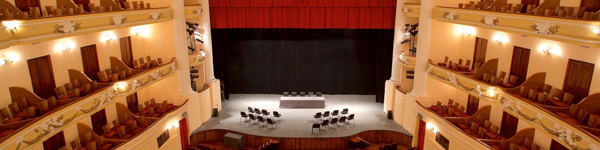 Un teatro majestuoso con cortinas rojas, varios palcos y hileras de asientos rojos.