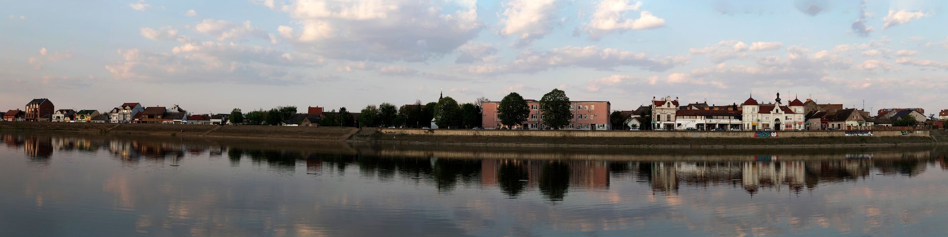 Un paisaje urbano a orillas del río, con edificios históricos y un cuerpo de agua tranquila que refleja el cielo.
