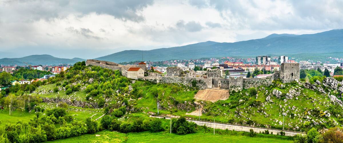 A historic castle on a hill overlooking a town with mountains in the background.