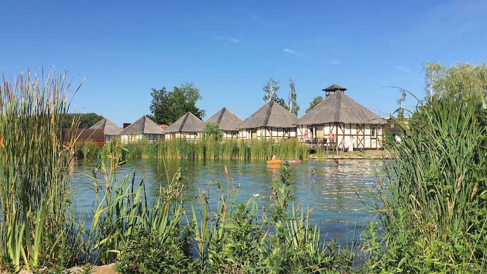 A serene lakeside with thatched-roof huts and lush greenery.