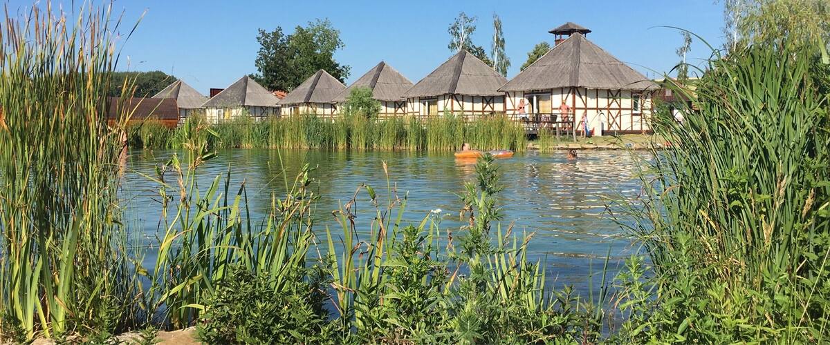 A serene lakeside with thatched-roof huts and lush greenery.