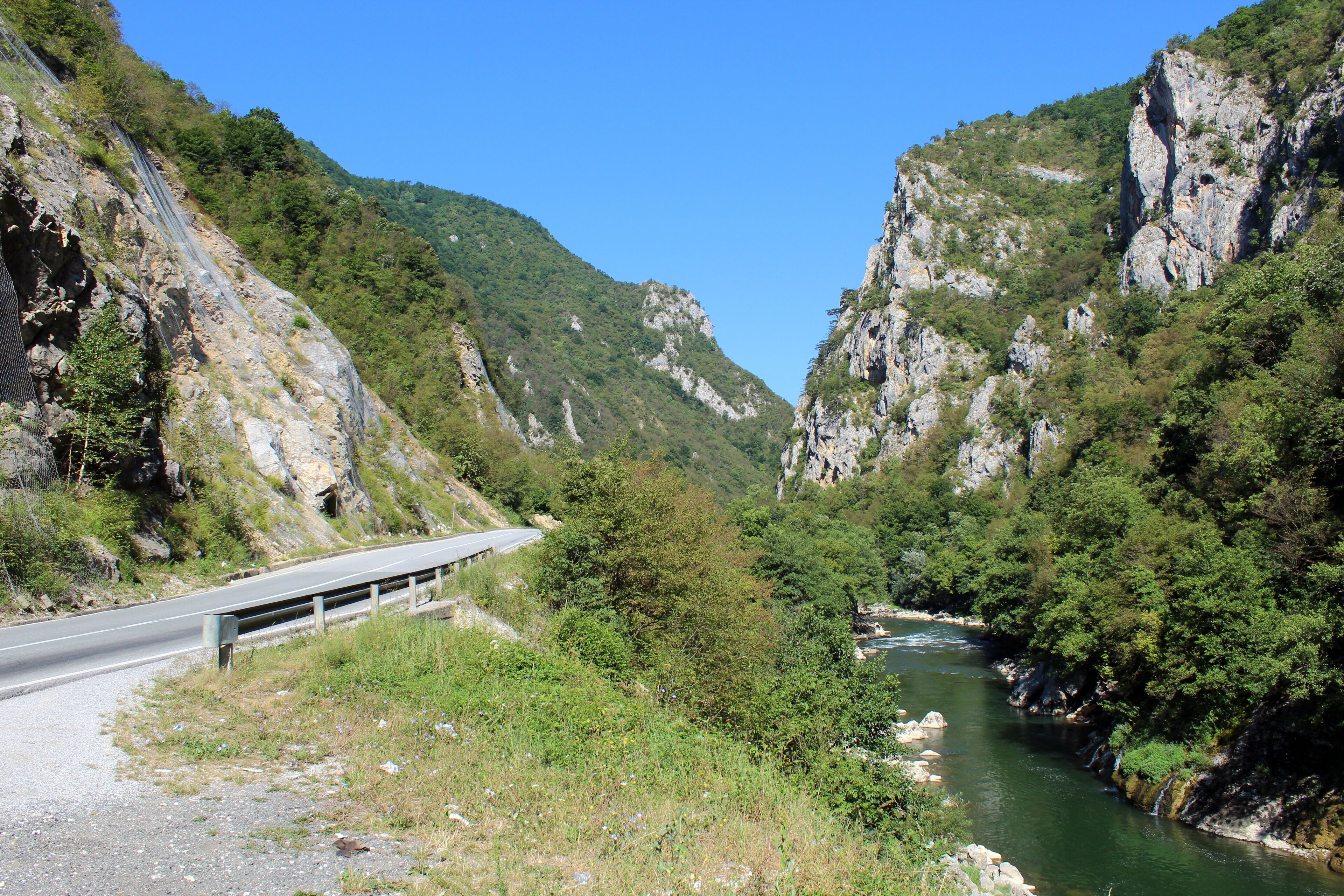 A winding road through a canyon with a river running alongside it.
