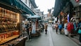 A bustling market street with traditional architecture and various stalls selling jewelry and clothing.