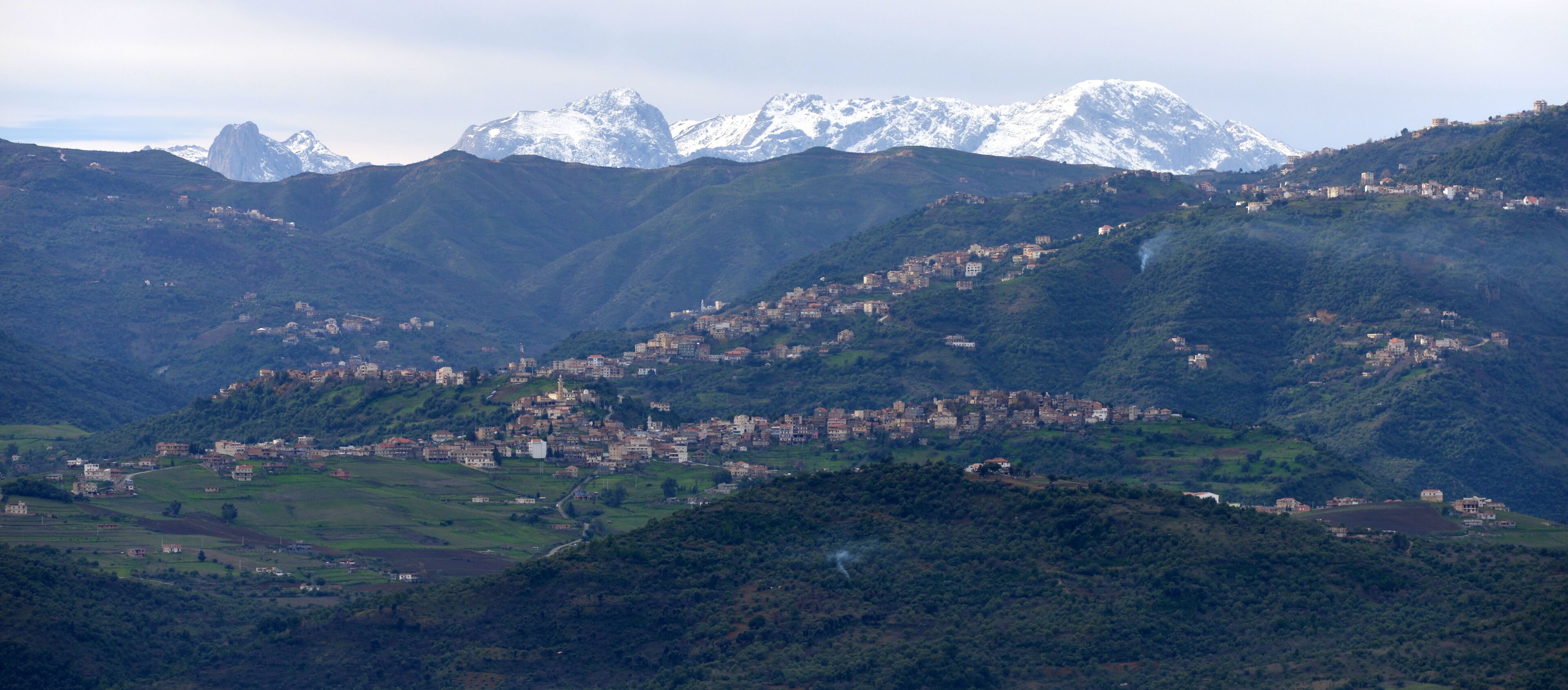 A mountainous landscape with a town nestled in the valley. Snow-capped peaks rise in the background.