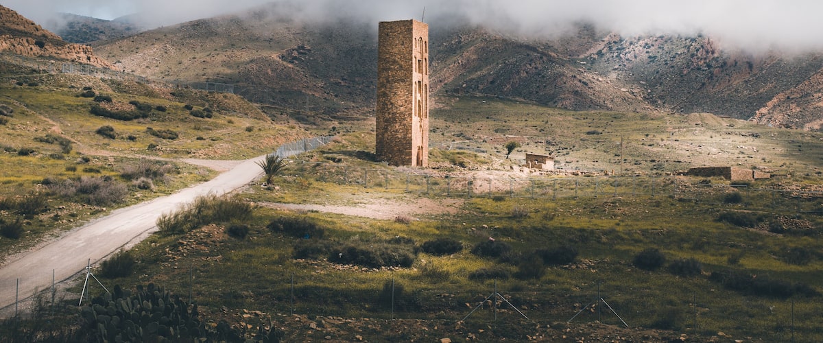 A solitary tower in a mountainous landscape with a dirt road leading to it.