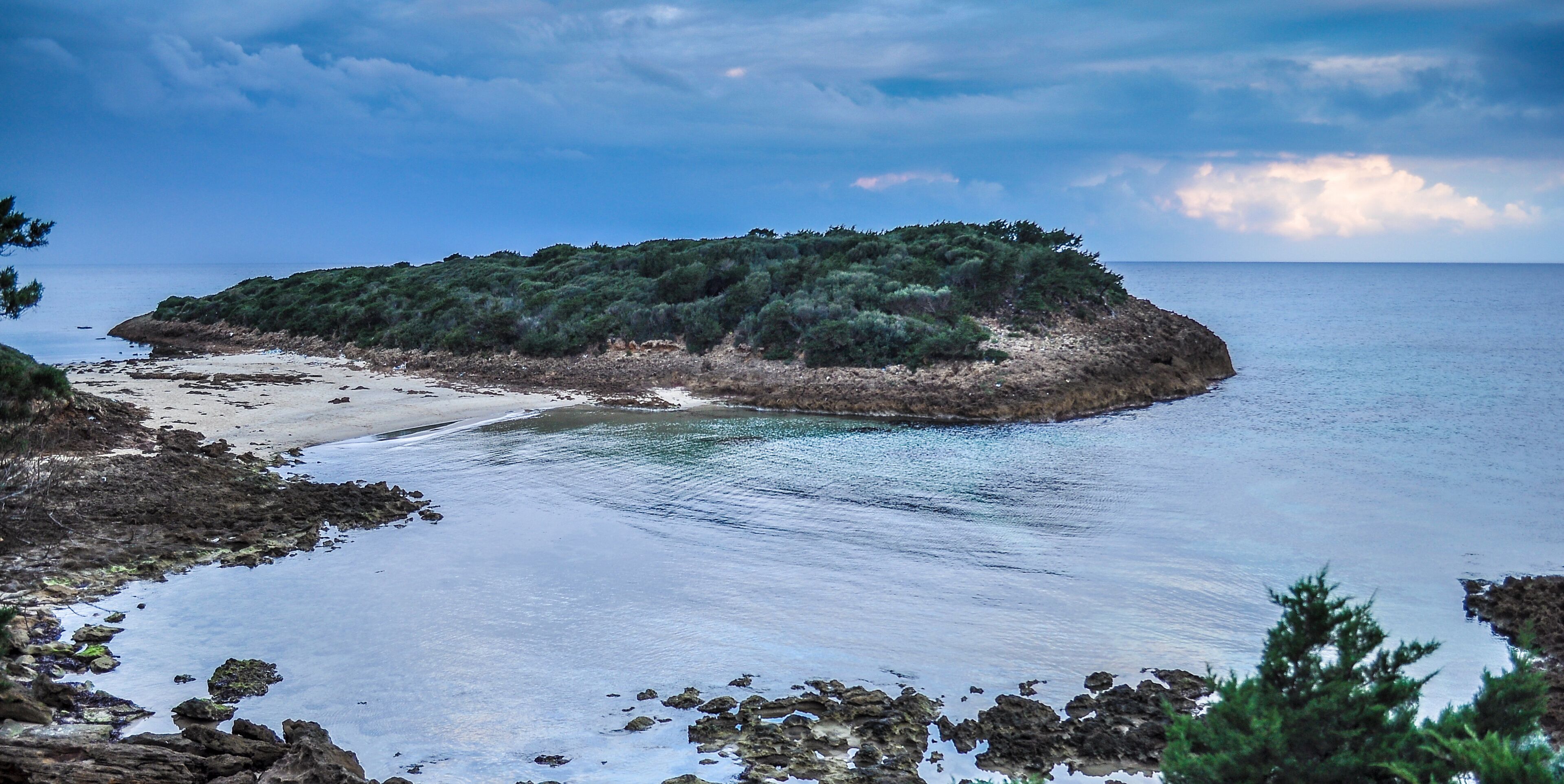 A coastal landscape with a small island covered in greenery, a sandy beach, and calm waters.