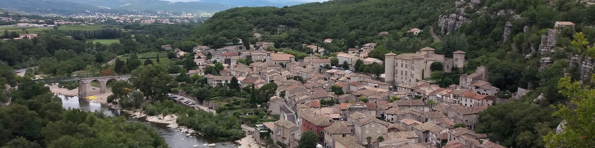 Un pueblo situado en un valle, con un río, rodeado de colinas y una estructura que parece un castillo.