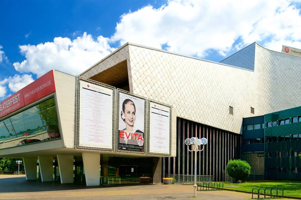 A modern theater building with a large billboard advertising a play.