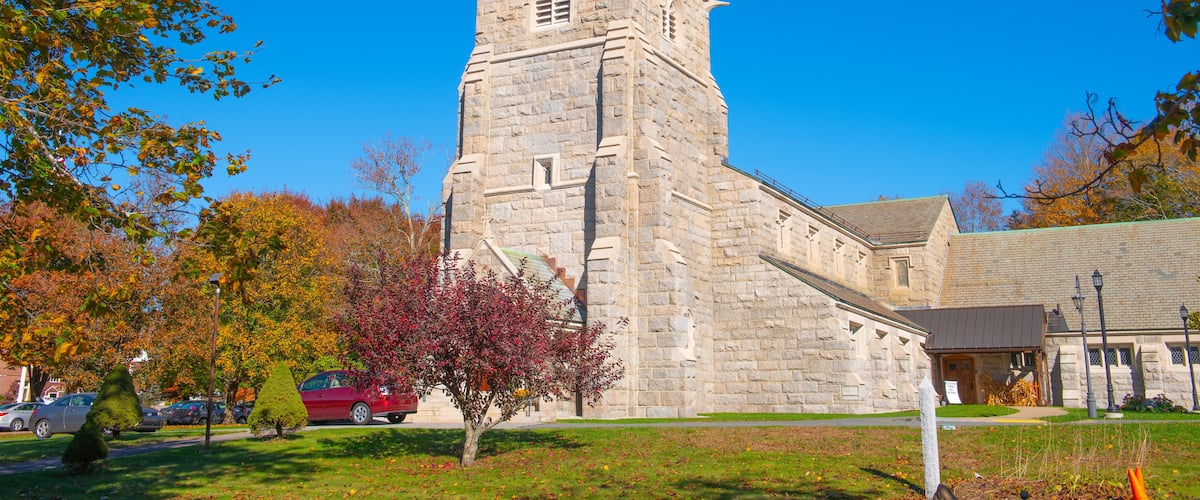 A stone church with a bell tower, surrounded by autumn-colored trees and a clear blue sky.
