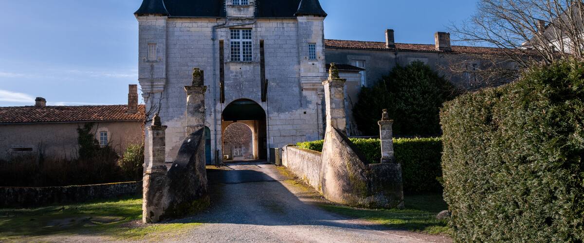 A historic stone building with a steeply pitched roof, a central archway, and a symmetrical facade.