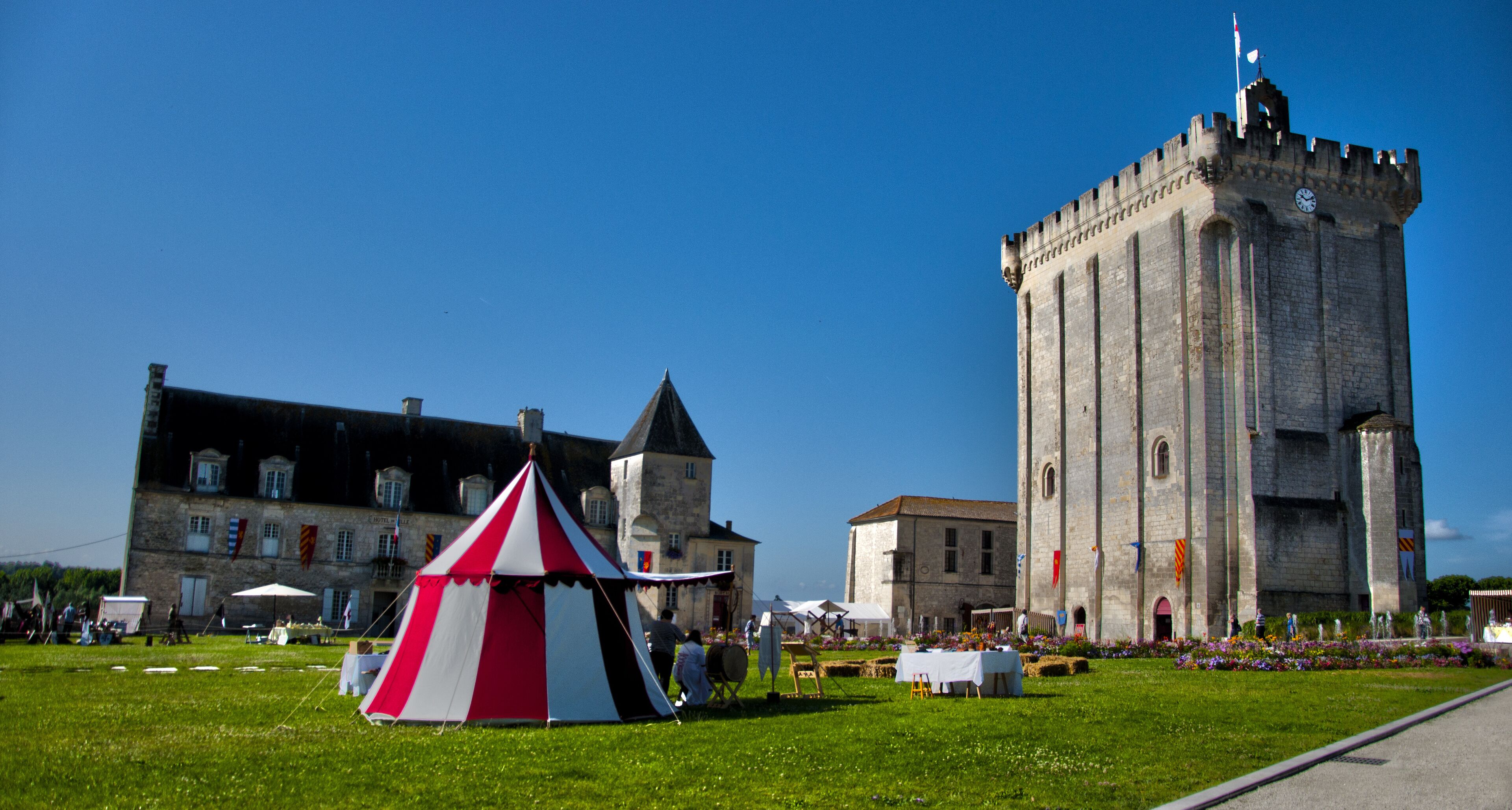 A castle with a clock tower and a red and white tent in a grassy field.