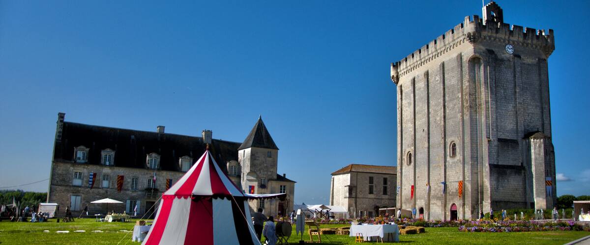 A castle with a clock tower and a red and white tent in a grassy field.