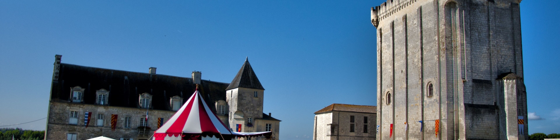 A castle with a clock tower and a red and white tent in a grassy field.
