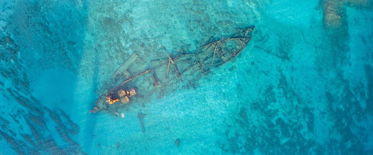 An aerial view of a sunken shipwreck with coral growth and clear turquoise waters.